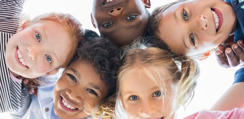 r and smiling at camera. Team of smiling kids embracing together in a circle. Portrait of young boy and pretty girls looking at camera.
