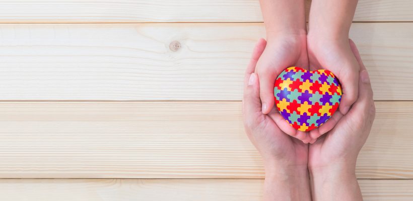 World Autism Awareness day, mental health care concept with puzzle or jigsaw pattern on heart with autistic child's hands supported by nursing woman, family caregiver person or parenting mother
